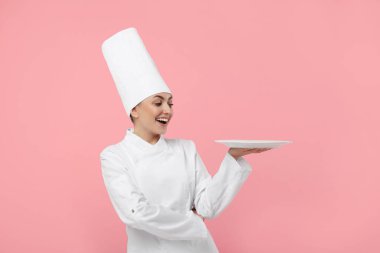 Üniformalı mutlu profesyonel pastacı pembe arka planda boş tabak tutuyor.