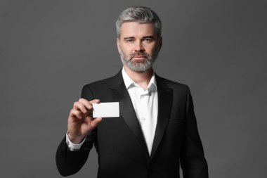Yakışıklı iş adamı gri arka planda boş kartvizit tutuyor.