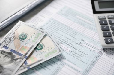 Maaş bordrosu. Vergi iade formu, hesap makinesi ve dolar banknotları masanın üzerinde, seçici odaklanma