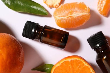 Aromatik mandalina yağı şişelerde ve turunçgiller beyaz masada, düz yerde.