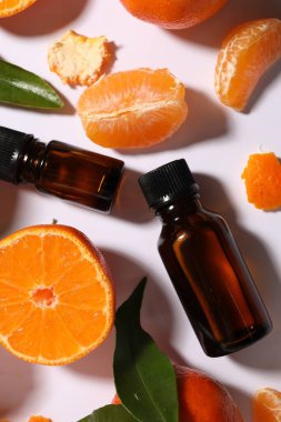 Aromatik mandalina yağı şişelerde ve turunçgiller beyaz masada, düz yerde.