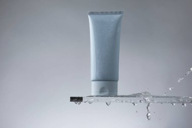 Cam üzerinde nemlendirici krem ve gri arka planda su damlaları.