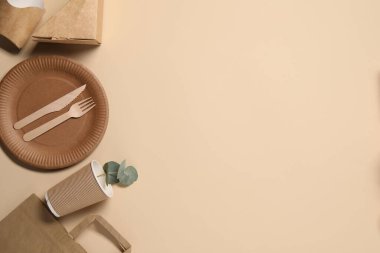 Çevre dostu gıda ambalajı. Kağıt kaplar, sofra takımı ve okaliptüs yaprakları bej arka planda, düz yerde. Metin için boşluk