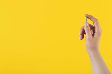 Sarı arka planda vitamin kapsülü tutan kadın, metin için yeri olan yakın plan. Sağlık takviyesi