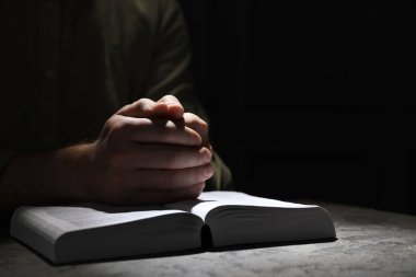 Religion. Christian man praying over Bible at table, closeup. Space for text clipart