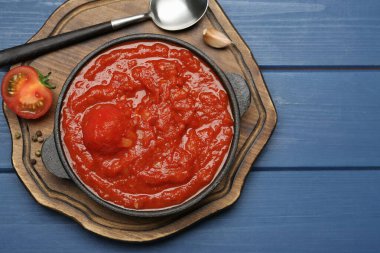 Ev yapımı domates sosu kasede, kaşık ve malzemeler mavi ahşap masada, üst tarafta.