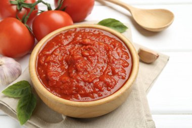 Ev yapımı domates sosu kasede, kaşıkta ve taze malzemeler beyaz ahşap masada, yakın plan.