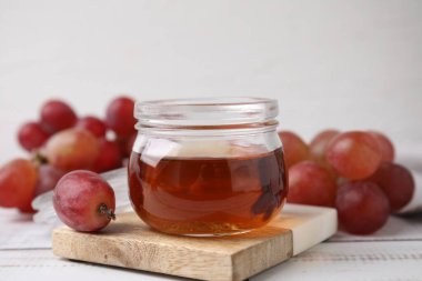 Cam kavanozda şarap sirkesi ve açık ahşap masada üzüm.