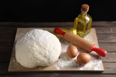 Çiğ hamur, merdane ve malzemeler ahşap masada.