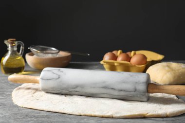 Çiğ hamur, merdane ve malzemeler gri masada.