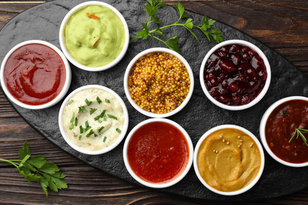 Different tasty sauces in bowls and parsley on wooden table, top view