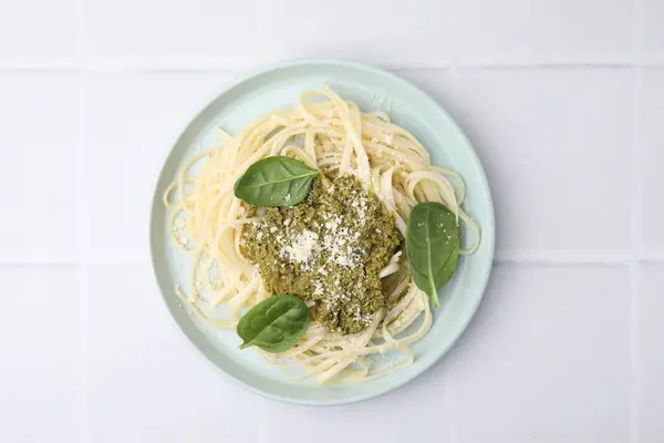 Tasty pasta with spinach, cheese and sauce on white tiled table, top view