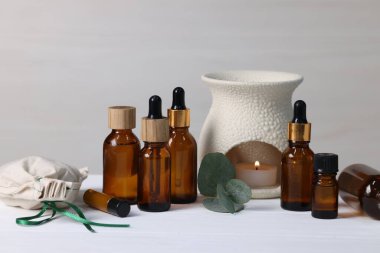 Farklı aromaterapi ürünleri, yanan mum ve okaliptüs yaprakları beyaz ahşap masa üzerinde ışık arka planına karşı