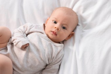 Beyaz çarşafların üzerinde uzanmış şirin bir bebek.