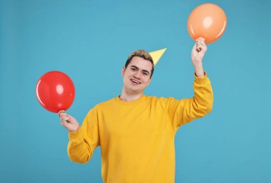 Parti şapkası ve açık mavi arka planda balonları olan genç bir adam.