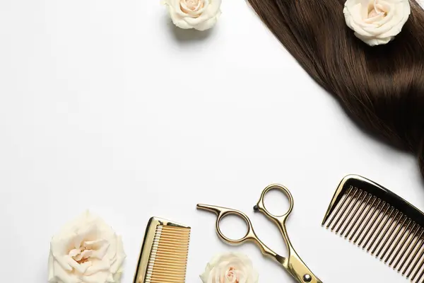 Hairdresser tools. Brown hair lock, combs, scissors and flowers on white background, flat lay. Space for text