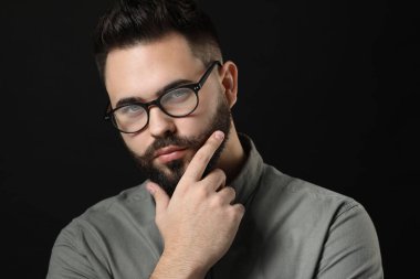 Bıyıklı genç adam siyah arka plana dokunuyor.