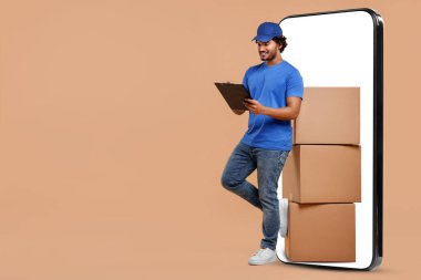 Koyu bej arka planda kocaman bir akıllı telefonun yanında paket ve pano yığını olan bir kurye. Teslimat servisi. Metin için boşluk