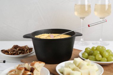Lezzetli peynirli fondü tenceresi, çatal, şarap ve beyaz ahşap masada farklı atıştırmalıklar.