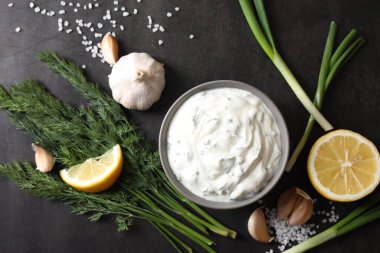 Dereotlu lezzetli yoğurt, yeşil soğan, limon ve sarımsak siyah arka planda, düz konum