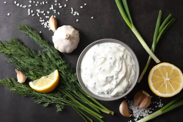 Dereotlu lezzetli yoğurt, yeşil soğan, limon ve sarımsak siyah arka planda, düz konum