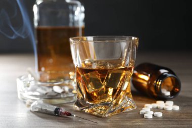 Alkol ve uyuşturucu bağımlılığı. Bardakta viski, şırınga, haplar ve sigaralar ahşap masada.