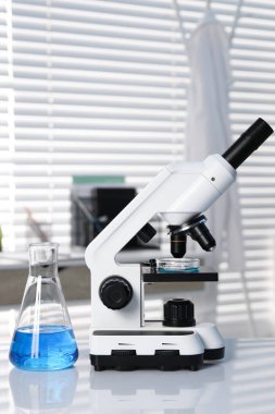 Laboratuvar analizi. Mavi sıvılı matara ve beyaz masada mikroskop