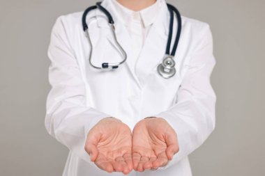 Steteskoplu doktor gri arka planda bir şey tutuyor, yakın plan.