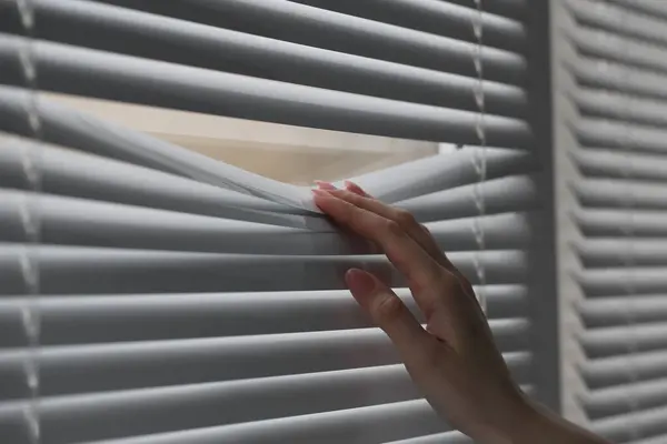 stock image Woman separating slats of white blinds indoors, closeup