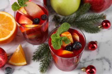 Aromatik Sangria içeceği bardaklarda, malzemelerde ve beyaz mermer masada Noel dekorunda.