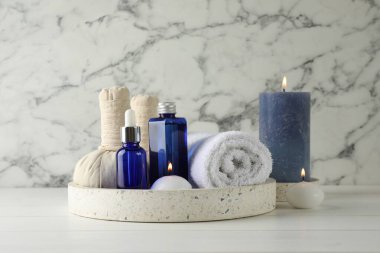 Spa kompozisyonu. Kozmetik ürünleri, havlu, bitkisel poşetler ve beyaz ahşap masada yanan mumlar.