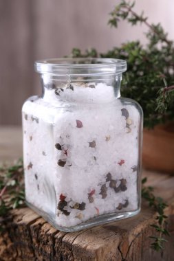 Cam kavanozda biberli tuz ve ahşap masada kekik, yakın plan.