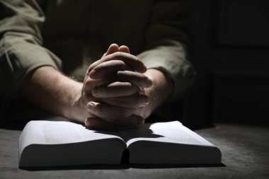 Din. Hıristiyan adam masada İncil için dua ediyor, yakın plan.