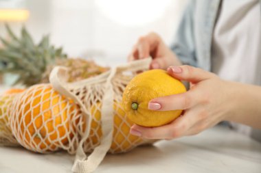 Elinde bir torba taze meyve ve limon olan kadın ışık masasında, yakın plan.