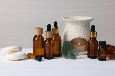 Farklı aromaterapi ürünleri, yanan mum ve okaliptüs yaprakları beyaz ahşap masa üzerinde ışık arka planına karşı