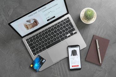 İnternetteki web sitesi laptop ekranında. Bilgisayar, akıllı telefon, kırtasiye, kredi kartı ve kaktüs gri masada, düz konum