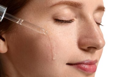Yüzüne beyaz arka planda kozmetik serumu süren çilli güzel bir kadın. Yakın plan.