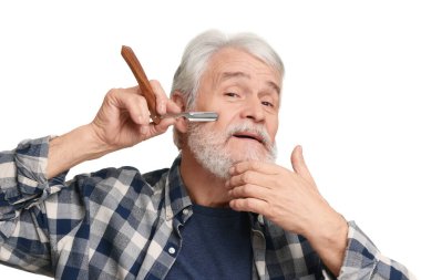 Yaşlı adam, beyaz arka planda bıçak ile sakal tıraşı oluyor.