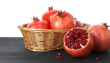 Hasır sepetin içinde taze nar, beyaz arka planda siyah ahşap masada.