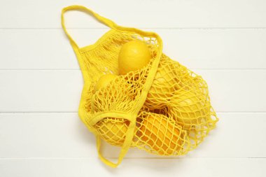Beyaz ahşap arka planda taze limonlu ip torbası, üst manzara.