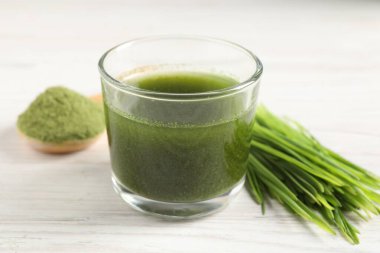 Buğday suyu bardakta ve beyaz ahşap masada taze lahanalar, yakın plan.