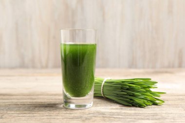 Buğday suyu shot bardakta ve ahşap masada taze yeşil lahanalar, yakın plan.