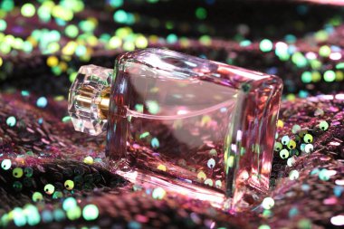 Renkli pullu kumaş üzerinde şişedeki lüks parfüm, yakın plan.