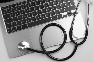 Açık gri arkaplanda dizüstü bilgisayar ve steteskop, düz konum