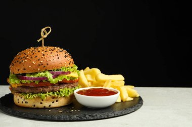 Lezzetli köfteli hamburger, patates kızartması ve gri masada sosla siyah arka plan, mesaj için yer.