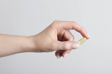 Açık gri arka planda vitamin kapsülü tutan kadın, yakın plan. Sağlık takviyesi