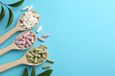 Kaşıklar içinde farklı vitamin hapları ve açık mavi arka planda yeşil yapraklar. Metin için boşluk