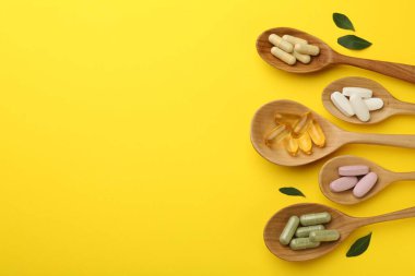 Kaşık içinde farklı vitamin hapları ve sarı arka planda yeşil yapraklar. Metin için boşluk