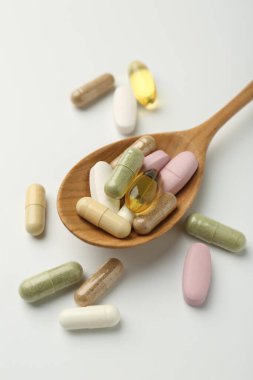 Beyaz arka planda kaşıkta farklı vitamin kapsülleri, yakın plan