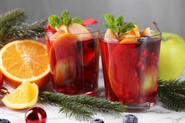 Aromatik Sangria içeceği bardaklarda, malzemelerde ve beyaz mermer masada Noel dekorunda.